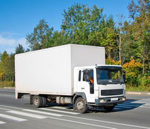 A white truck is driving down a road with trees in the background.