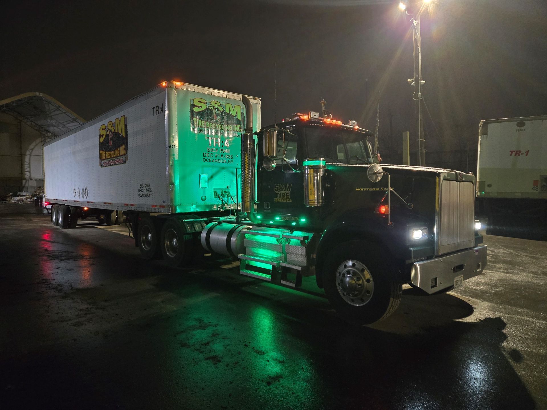 A semi truck is parked in a parking lot at night.