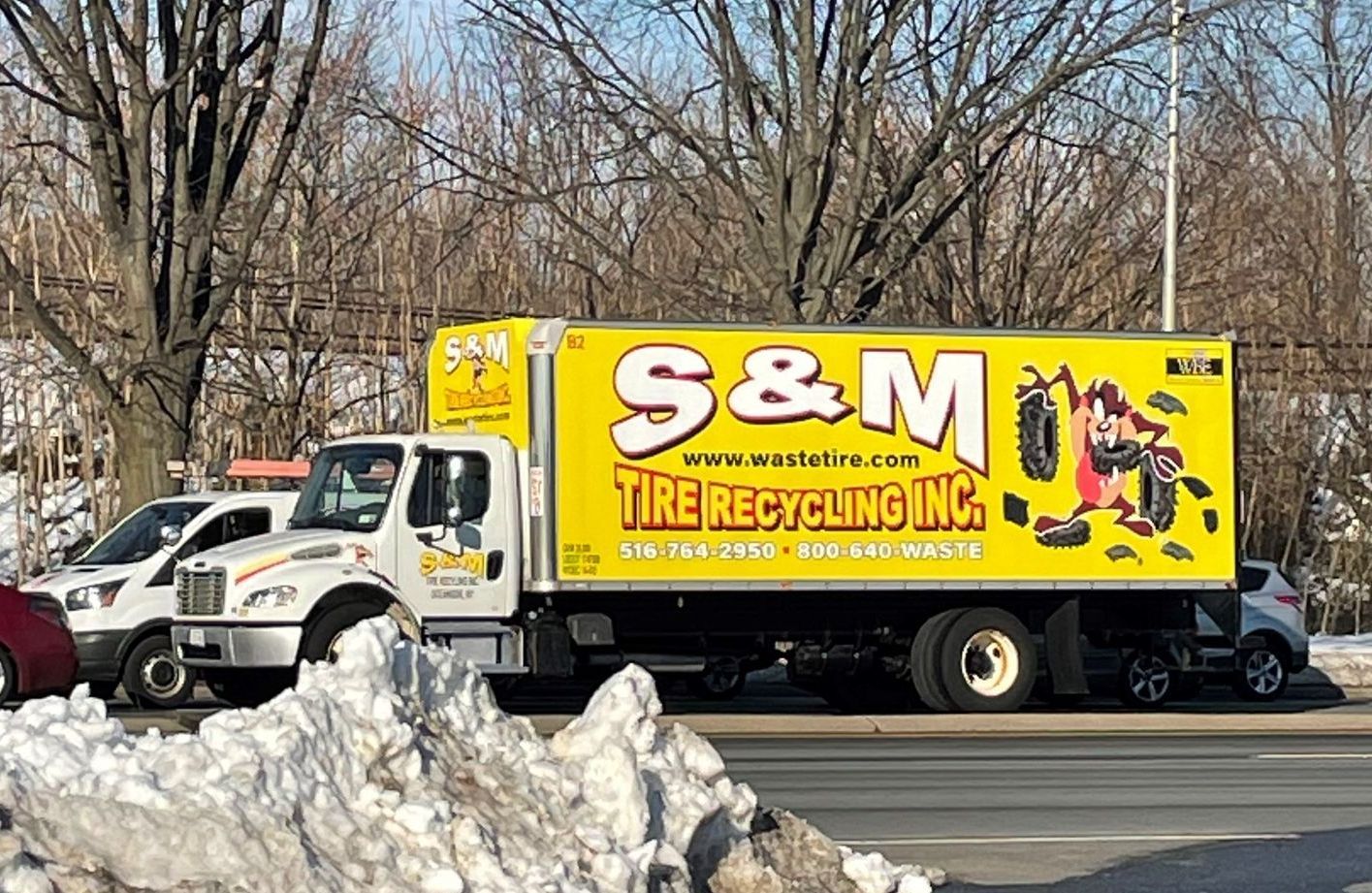 A white truck is driving down a road with trees in the background.