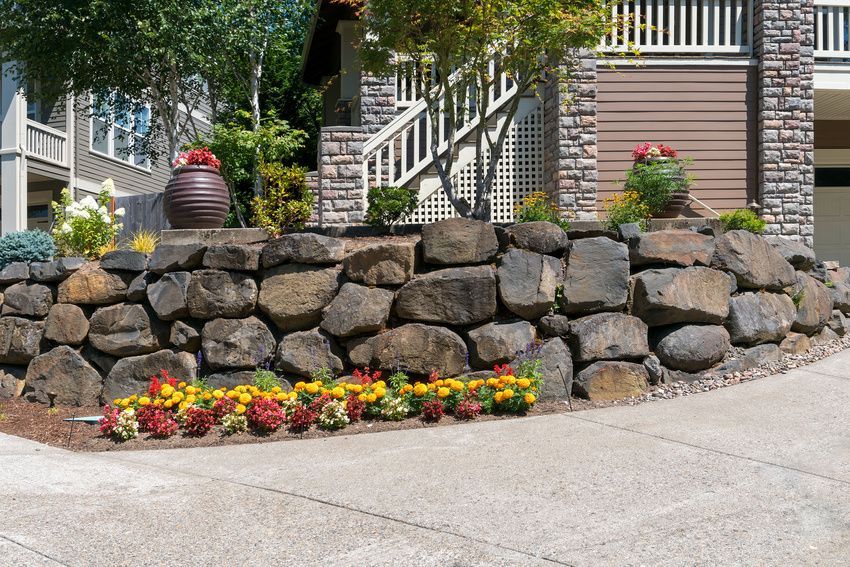 A large rock wall with flowers in front of a house