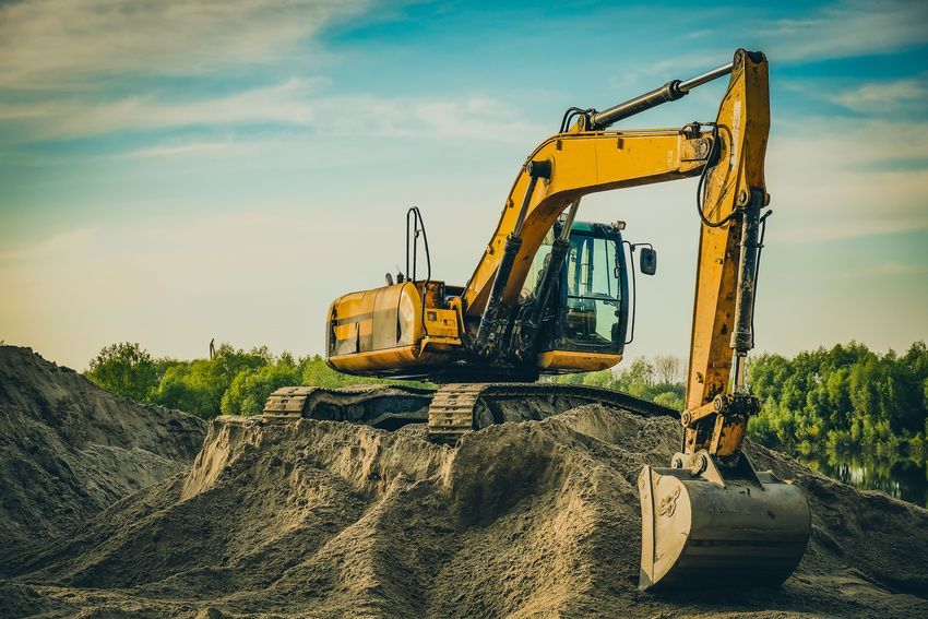 A yellow excavator is sitting on top of a pile of dirt.