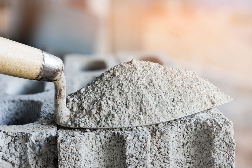 A person is pouring cement into a trowel on a brick.