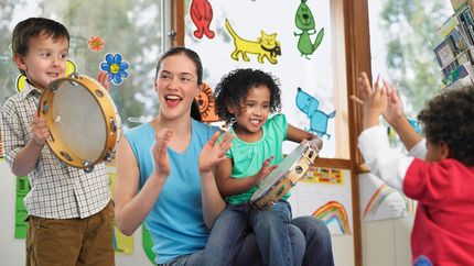 Adult and children playing music together in a bright classroom with colorful wall decorations