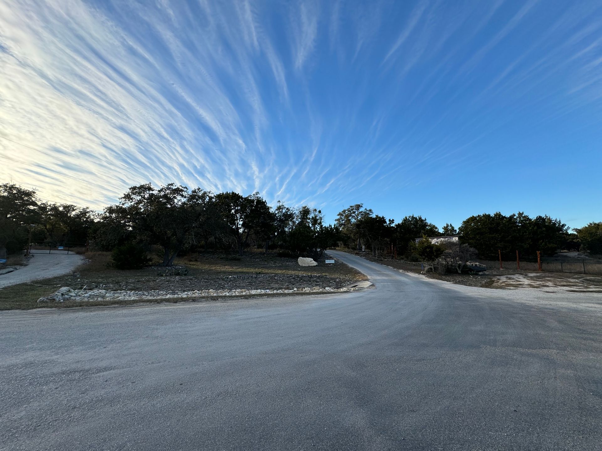 An RV park road with trees on both sides and a blue sky with clouds.