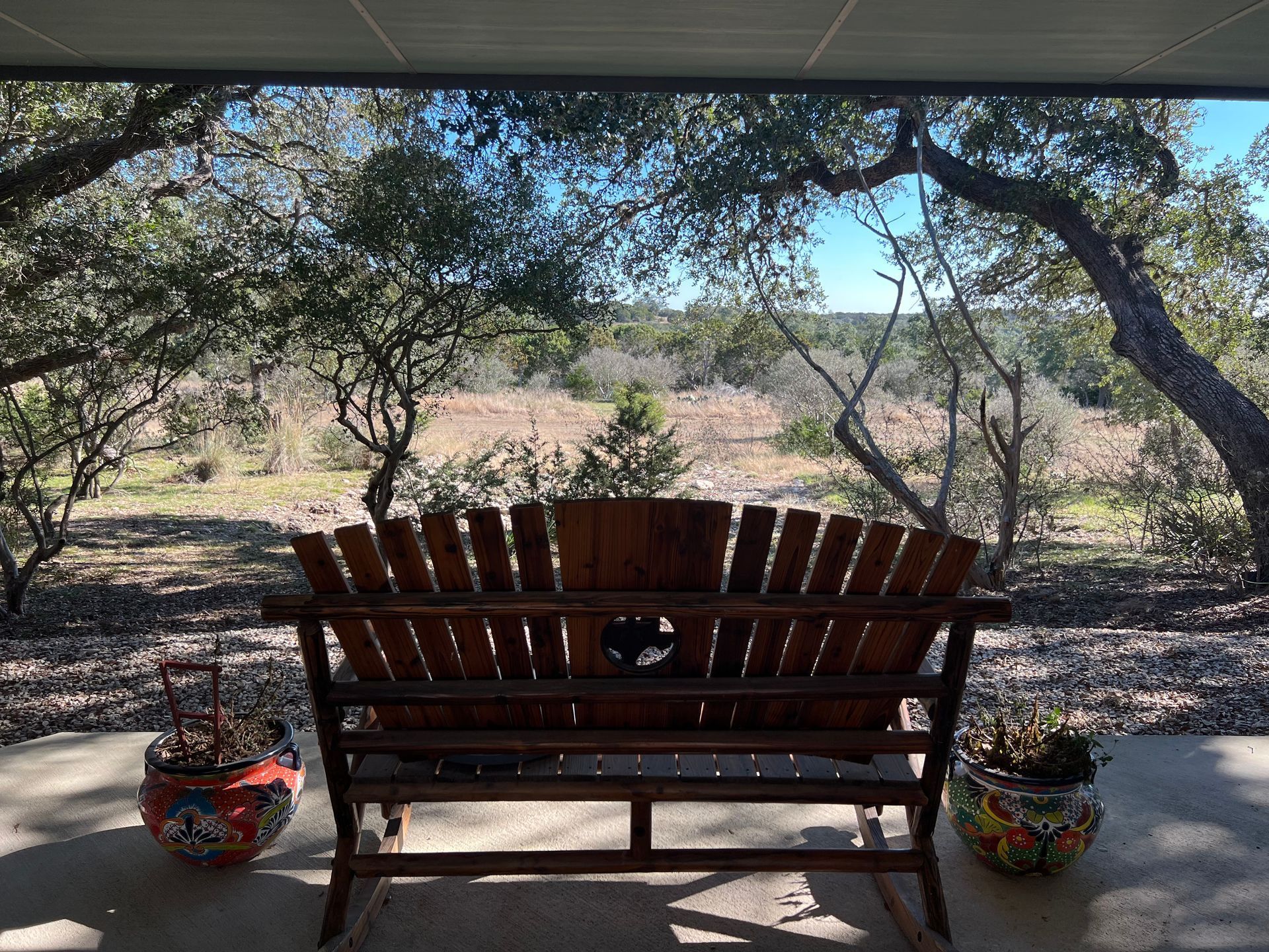 A wooden rocking bench on a porch with a view of a field.