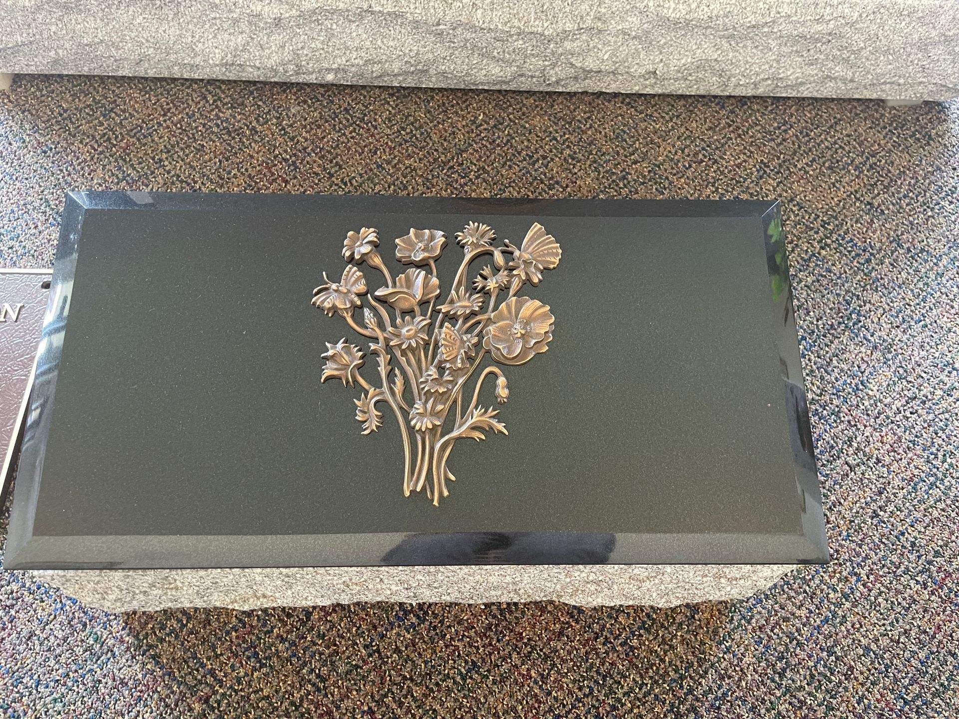 Black granite headstone with bronze floral design.