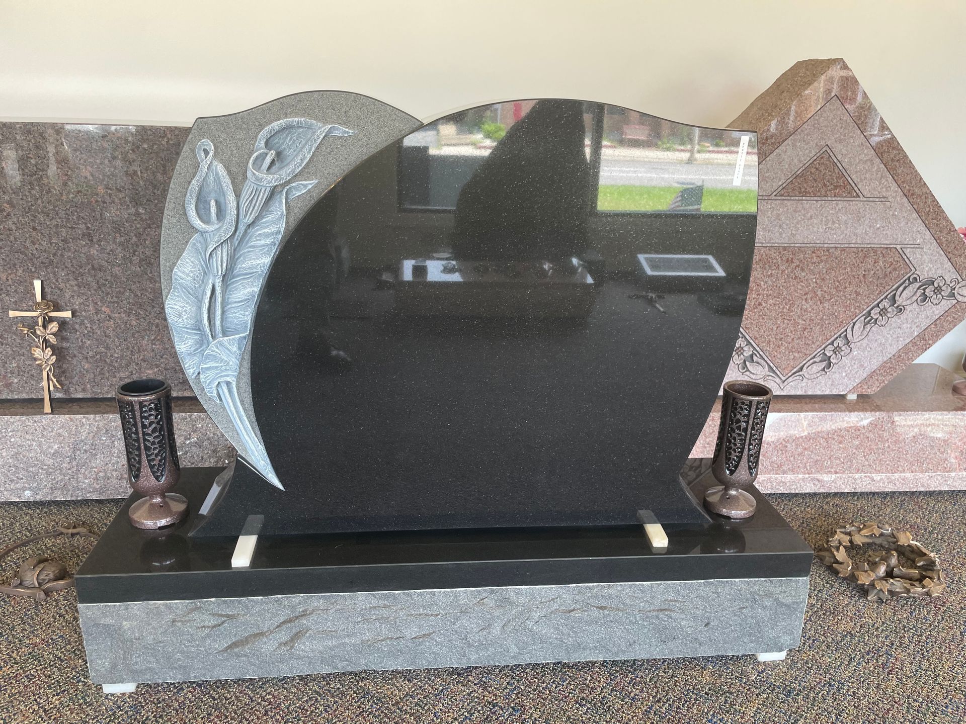 Black granite headstone with a carved floral design, resting on a gray base, with two vases.