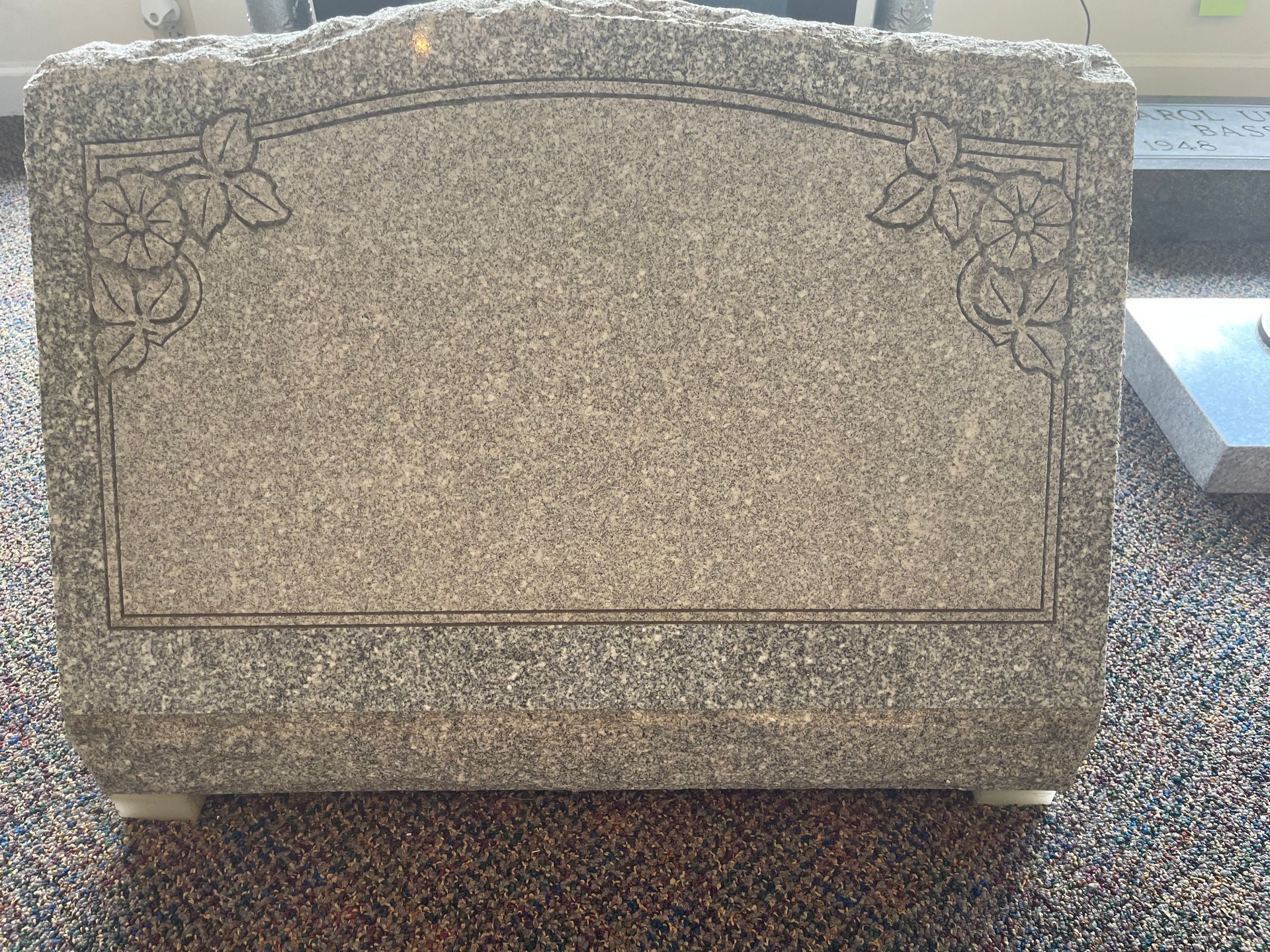 A light gray granite headstone with etched floral corner designs, ready for inscription.