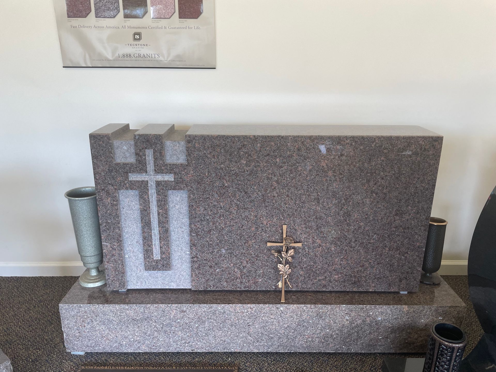A large granite headstone with a cross design, two vases, and a small crucifix on the front. Brown and gray tones.