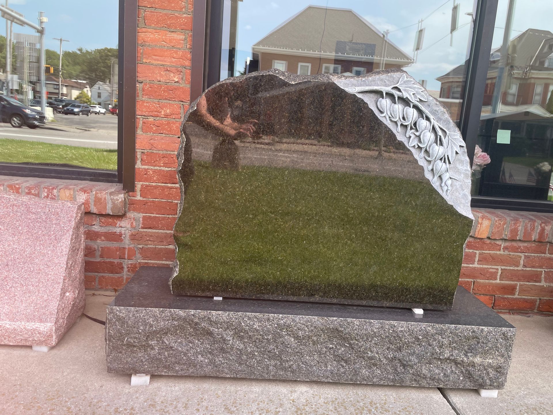 Black granite monument with a carved design, sitting on a gray granite base outside a brick building.
