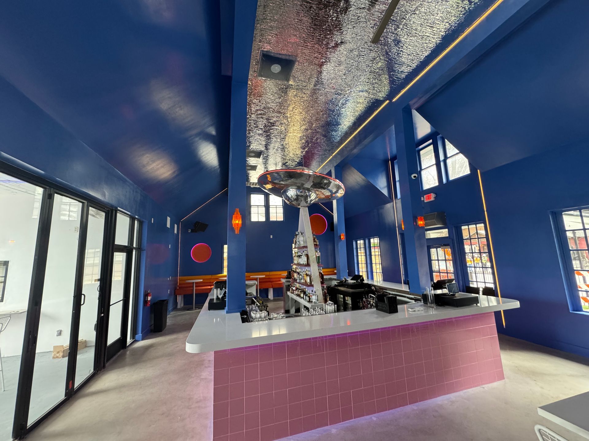 Brightly painted bar with a pink tiled facade, silver ceiling, and blue walls.