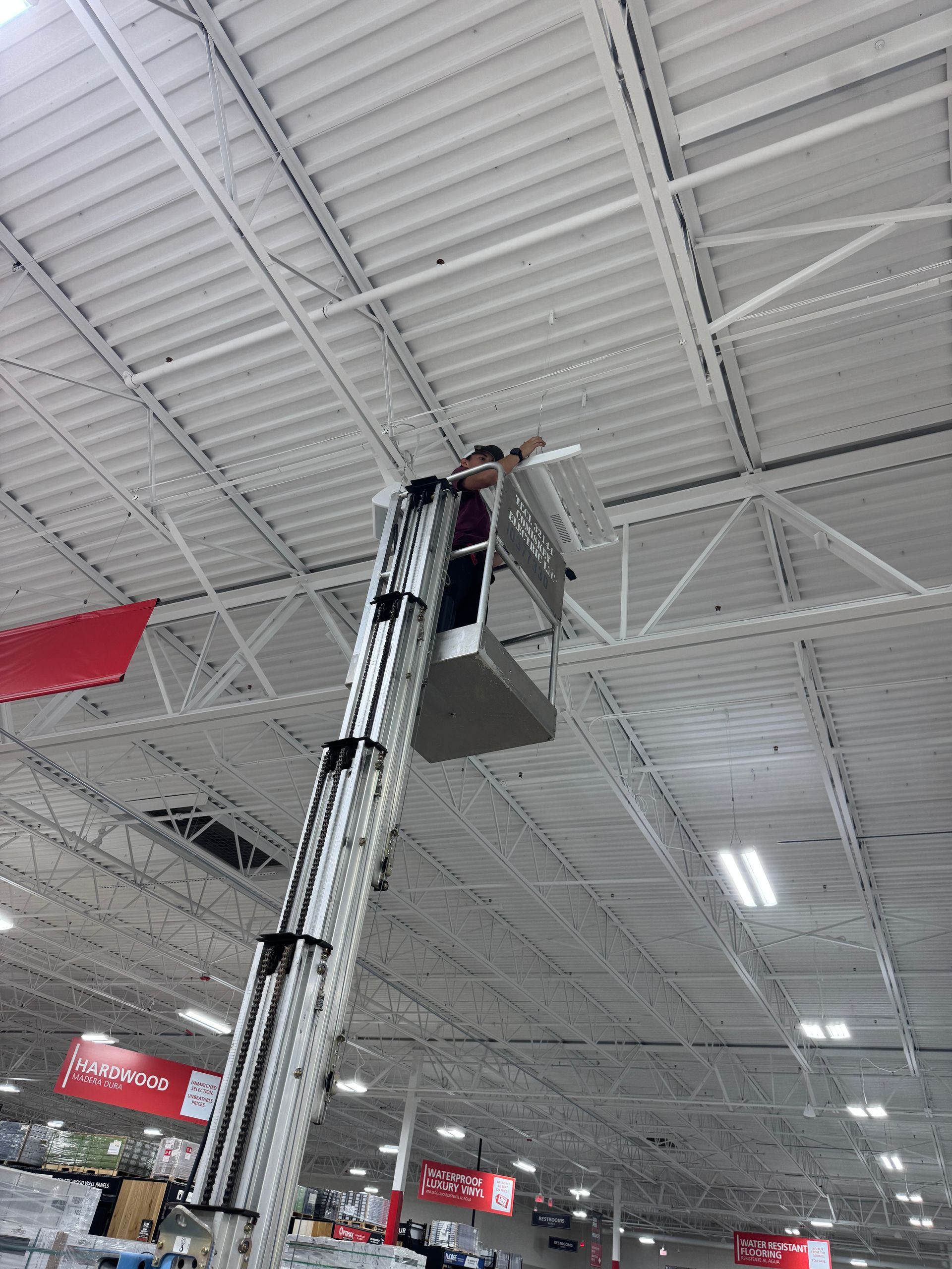 Person in a lift working on the ceiling of a large retail store.