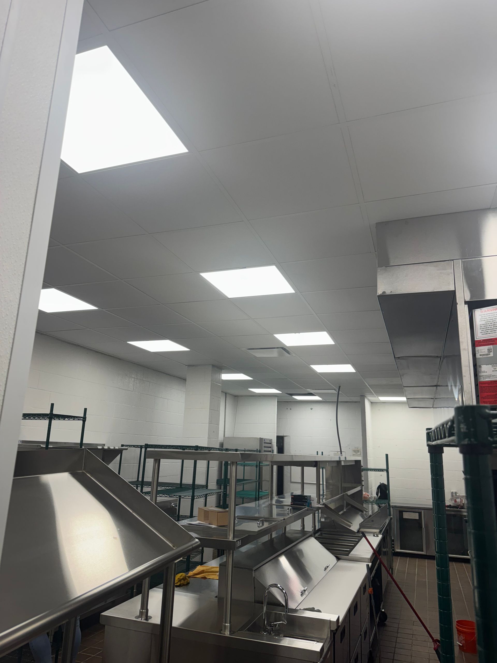 Commercial kitchen with stainless steel counters, shelves, and recessed ceiling lights.