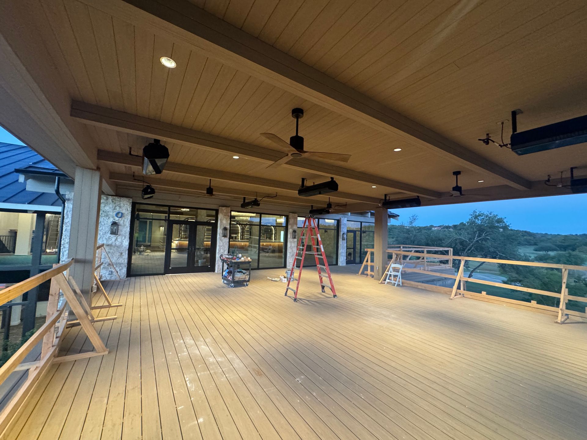 Covered outdoor deck with ceiling fans, lights, and ladder; overlooking a landscape.