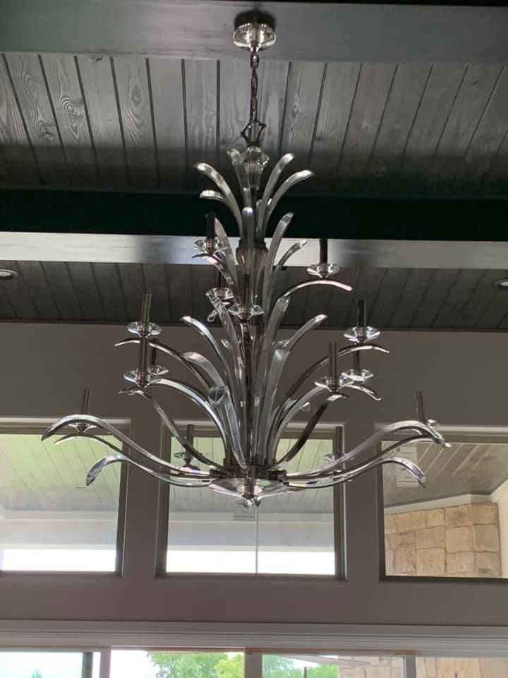 Silver chandelier hanging from a dark wood ceiling. Large windows below.