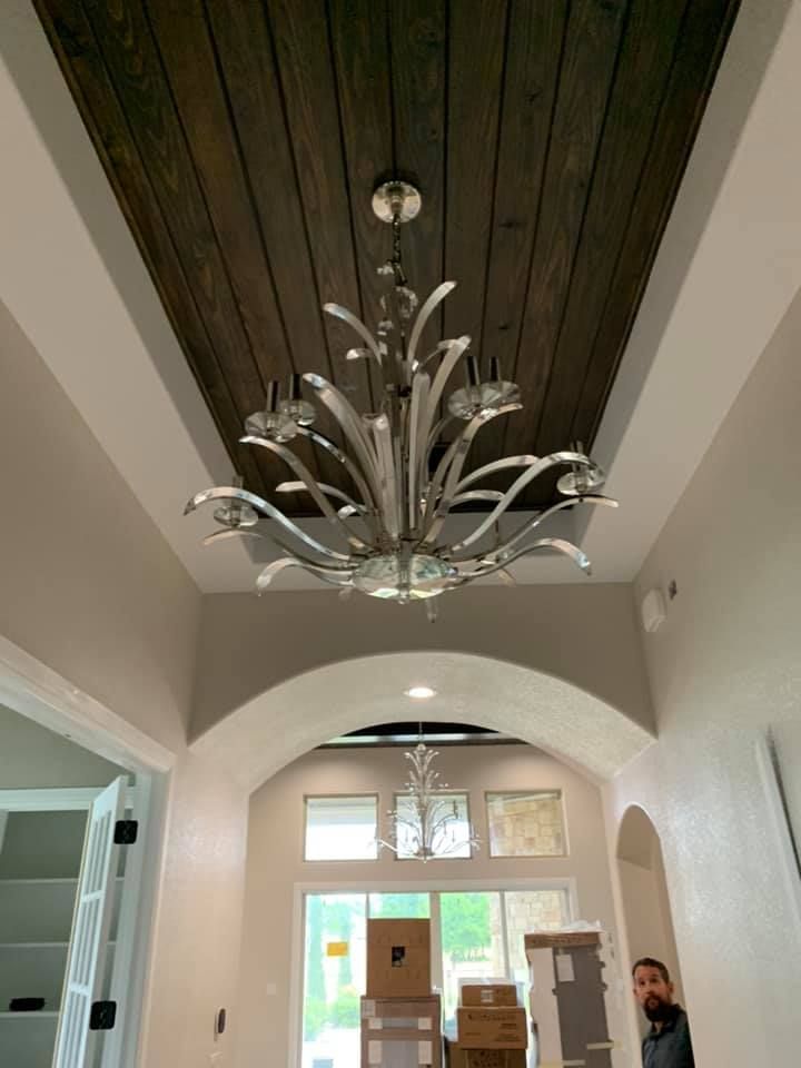 Silver chandelier hangs in a recessed, wood-paneled ceiling. Room with archways, boxes, and a man.