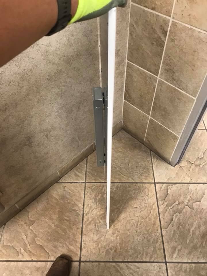 Person's hand holding a white, narrow panel, likely a door, in a tiled bathroom, pointing downward.