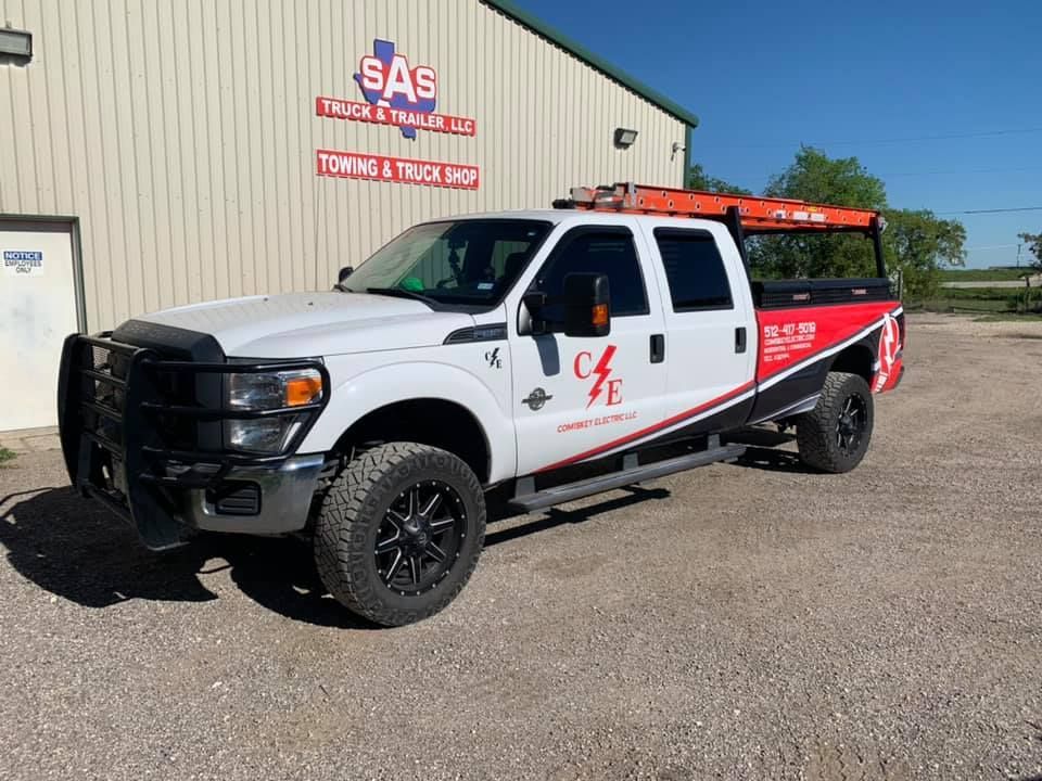 White pickup truck with black accents parked outside a towing and truck shop on a sunny day.