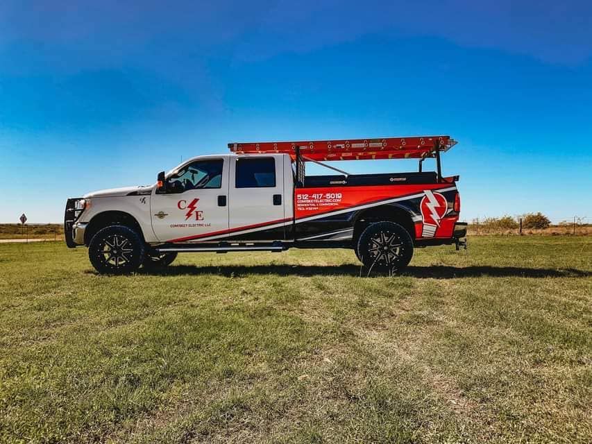 White pickup truck with company logo parked in a field, ladder on top, under a blue sky.
