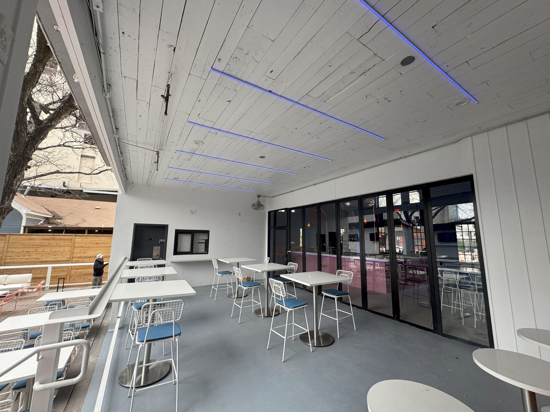 Outdoor restaurant patio with tables, chairs, and closed glass doors. Blue and white colors are present.