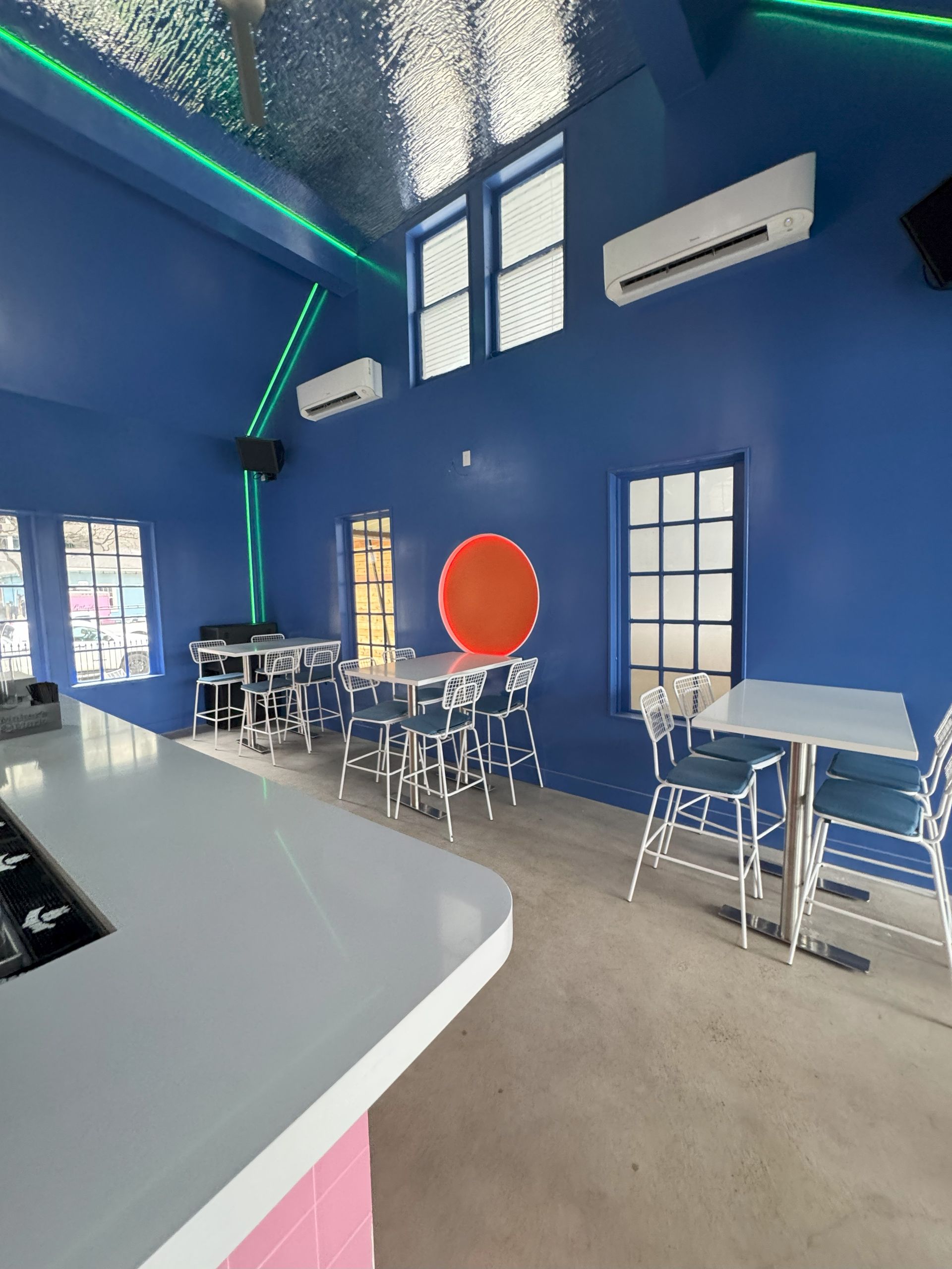Bright blue interior with tables, a white bar, and an orange circle on the wall.