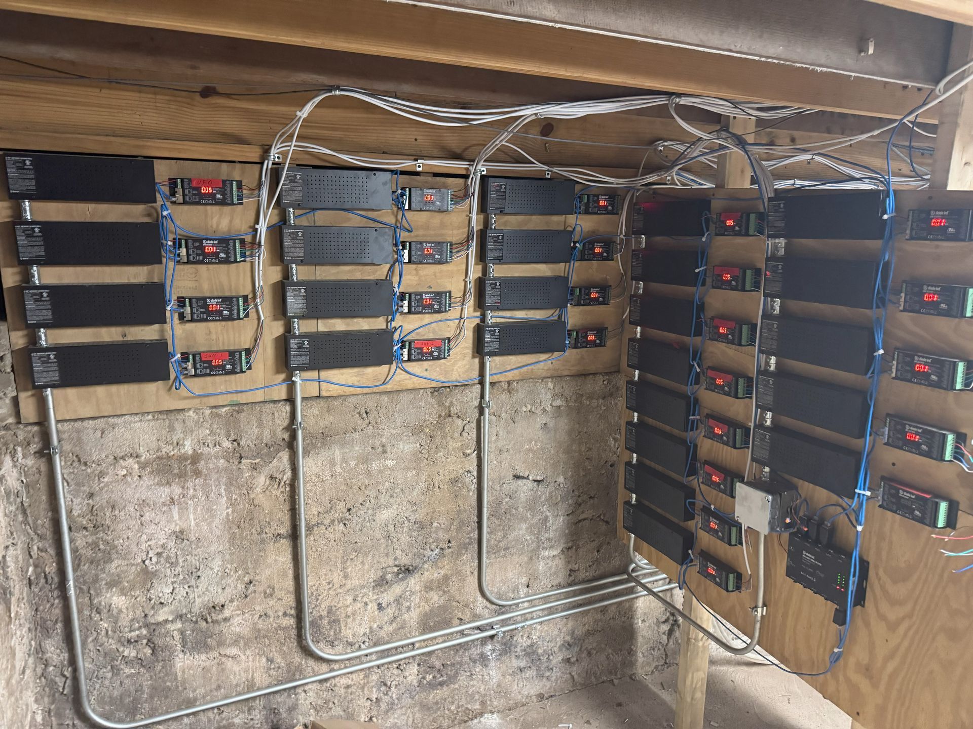 Electrical components mounted on wood boards, with many wires and a concrete wall background.