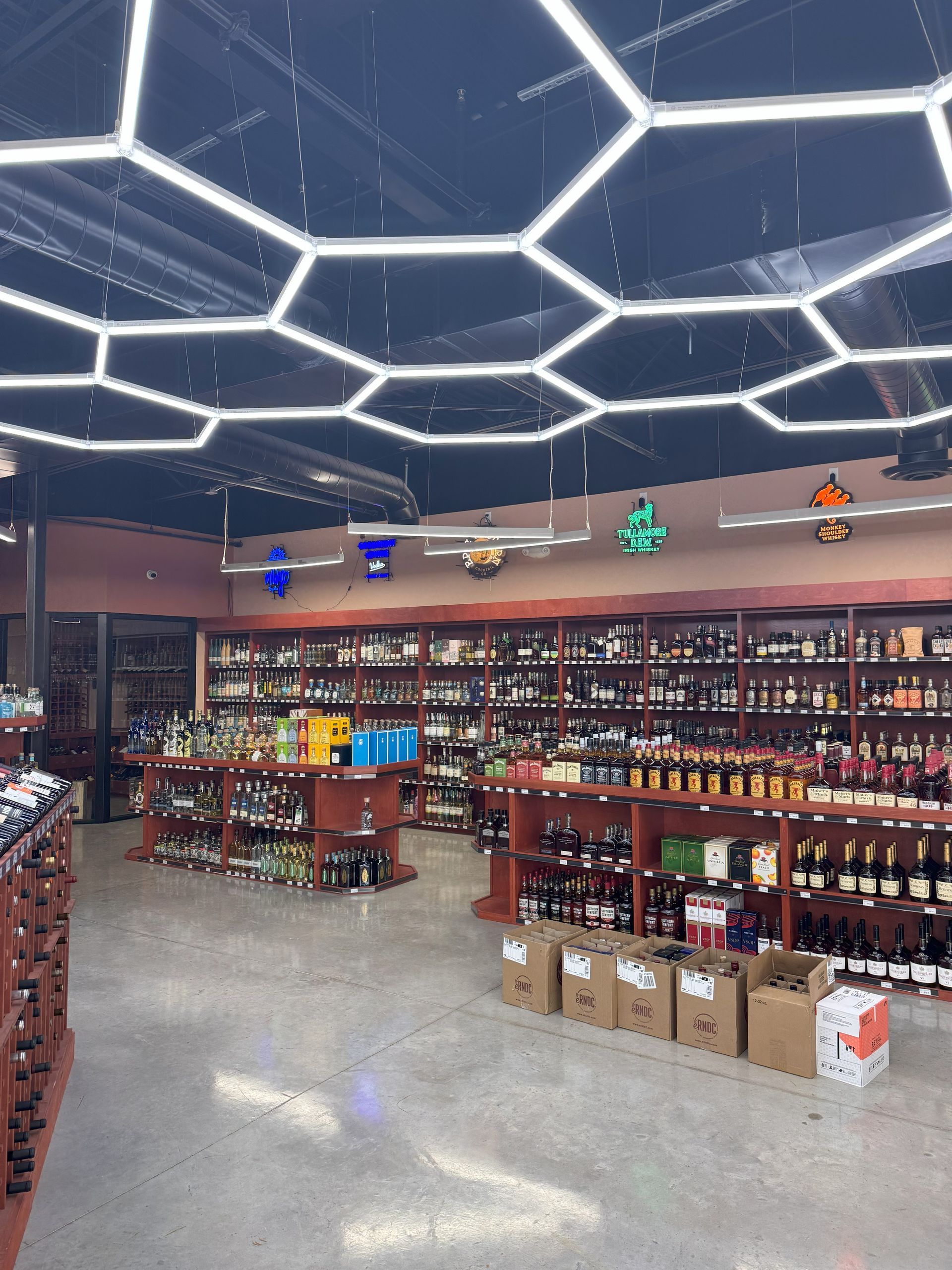 Liquor store interior with shelves stocked with bottles and hexagon-shaped ceiling lights.