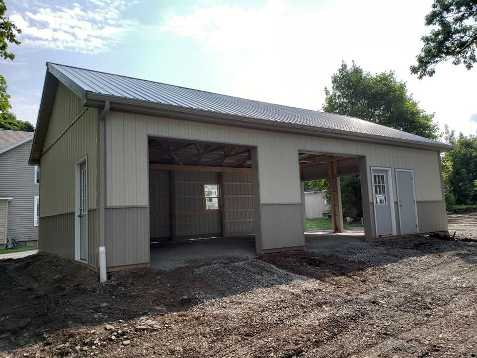 A large white building with a gray roof is sitting in the middle of a dirt field.