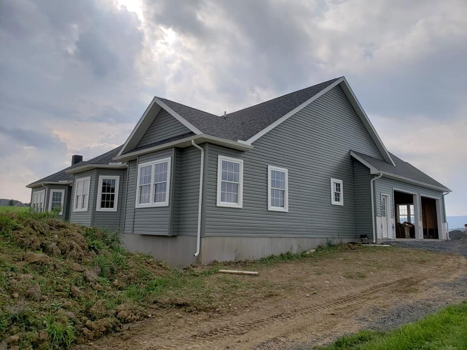 A large gray house is sitting on top of a dirt hill.