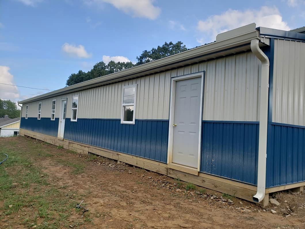 A blue and white building with a door and windows is sitting on top of a dirt field.