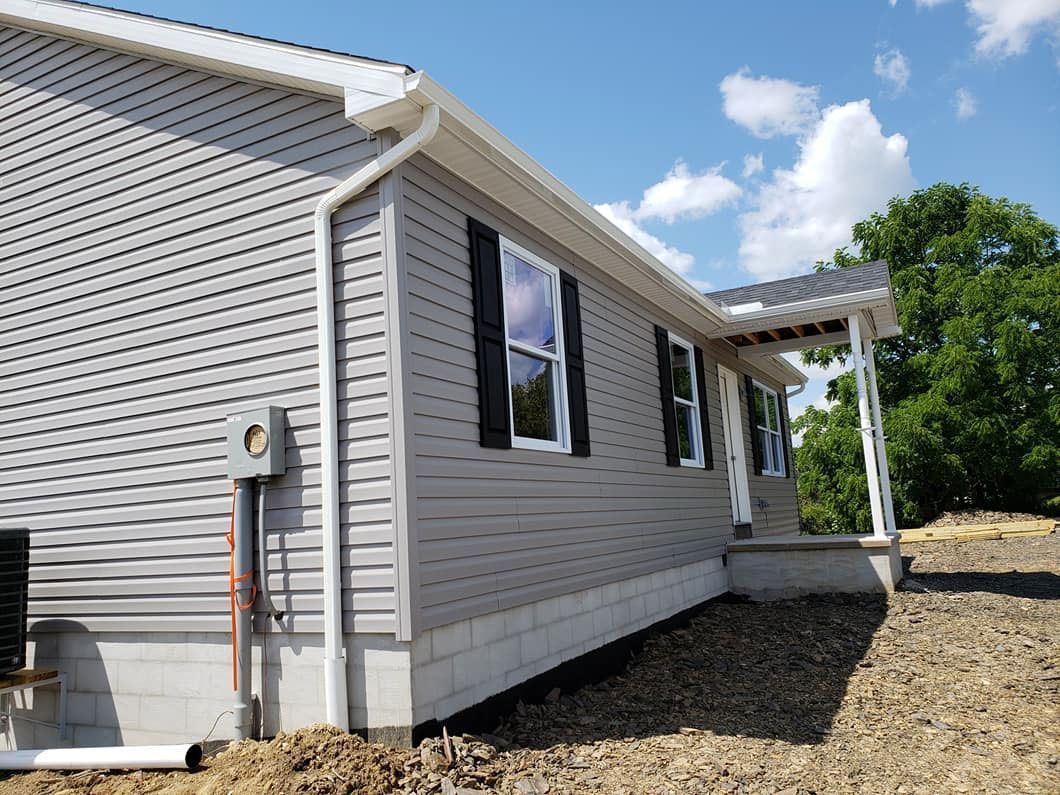 The side of a mobile home with black shutters and a porch.