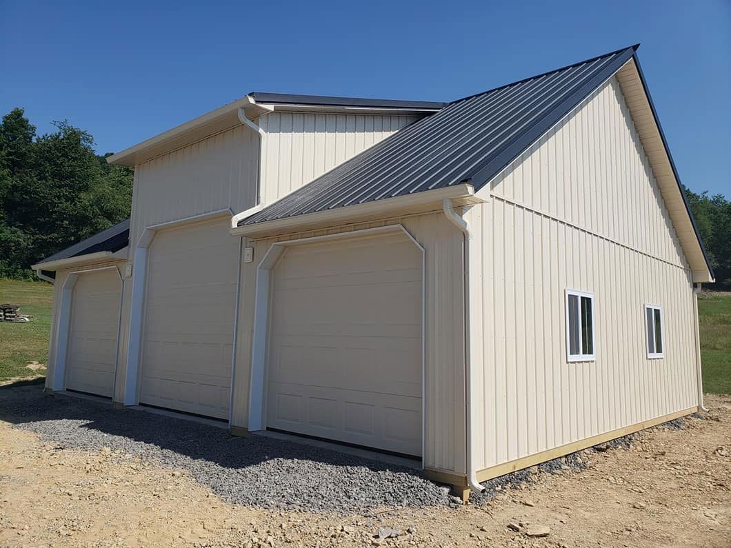 A white garage with a black roof is sitting in the middle of a dirt field.