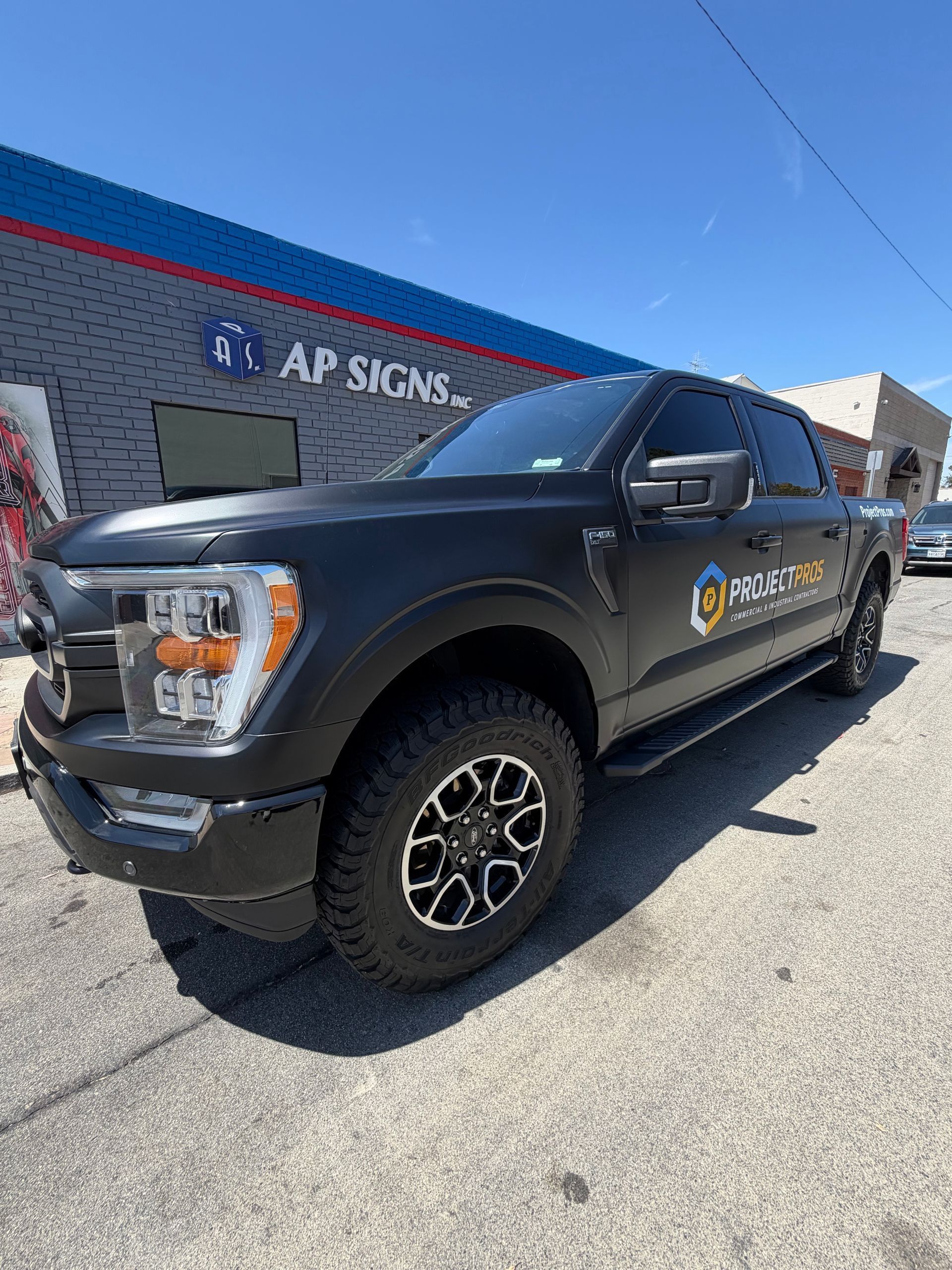 Black pickup truck with company logo parked outside an AP Signs building on a sunny day