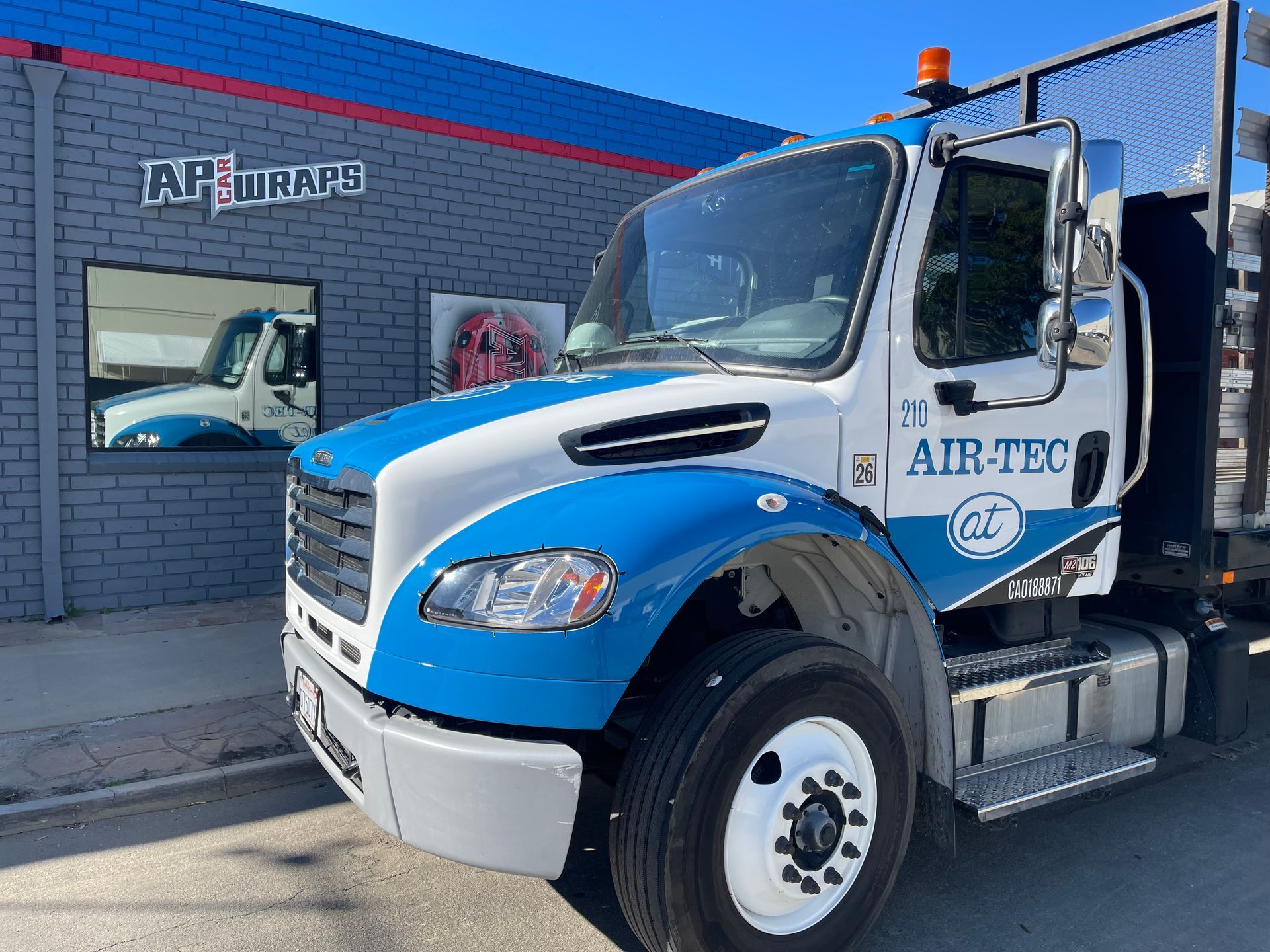 Blue and white AIRTEC utility truck parked outside a brick building with a large garage door