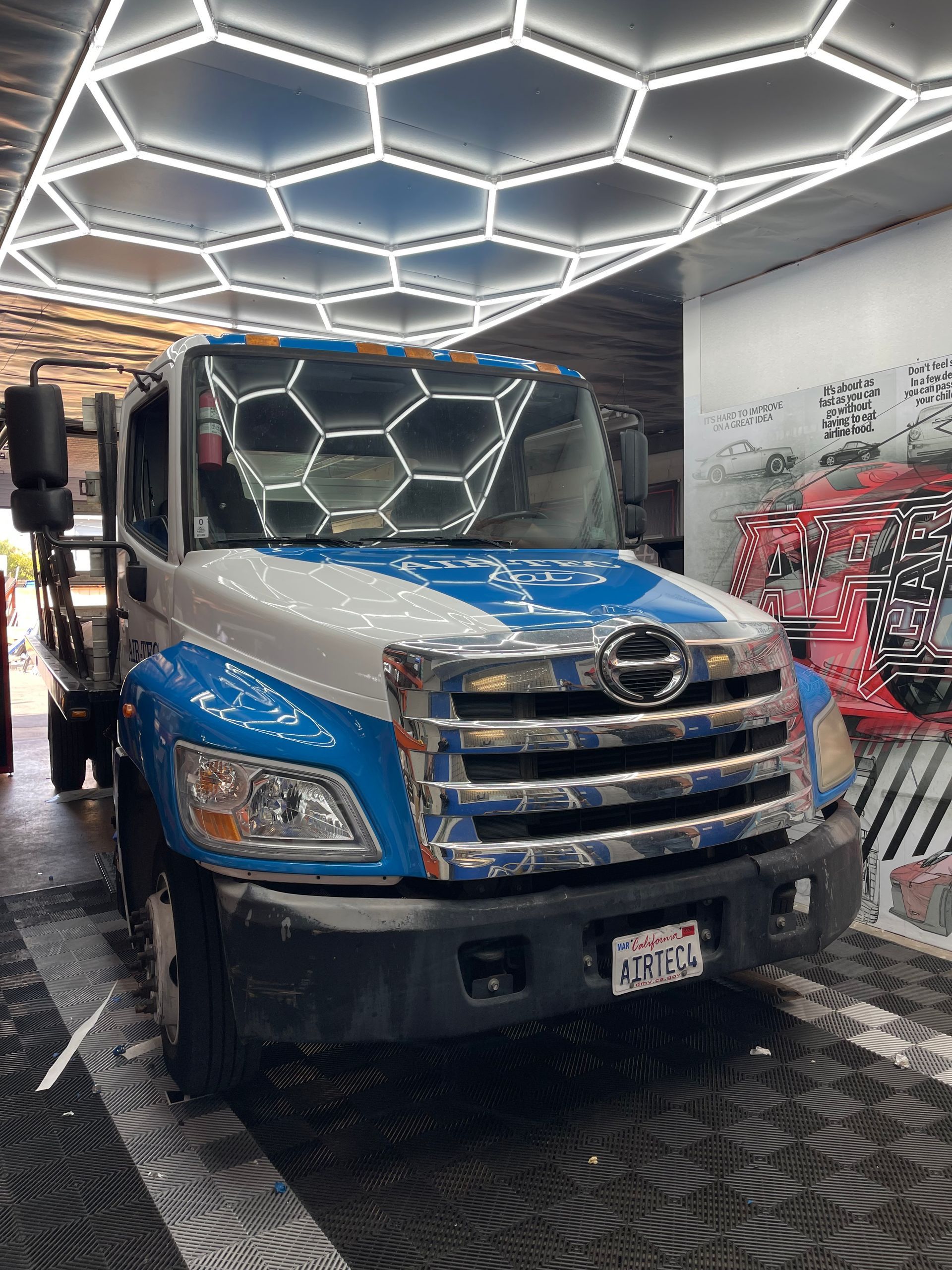 Blue truck parked indoors under hexagonal LED ceiling lights in a showroom or garage