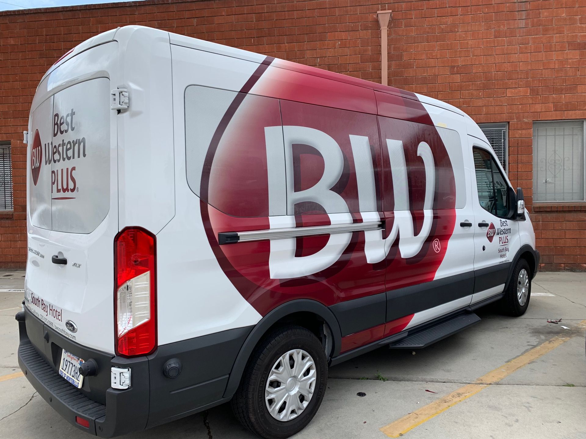 White Bud Light delivery van with large red-and-white logo parked beside a brick building.