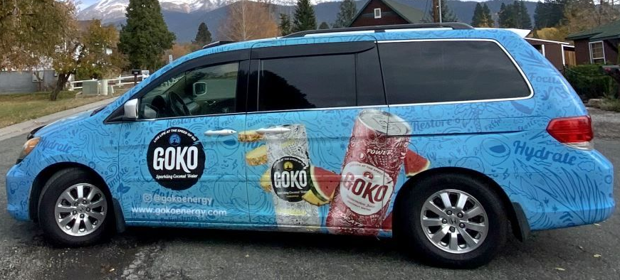Blue van with large can graphics and colorful advertising wrap parked on a street