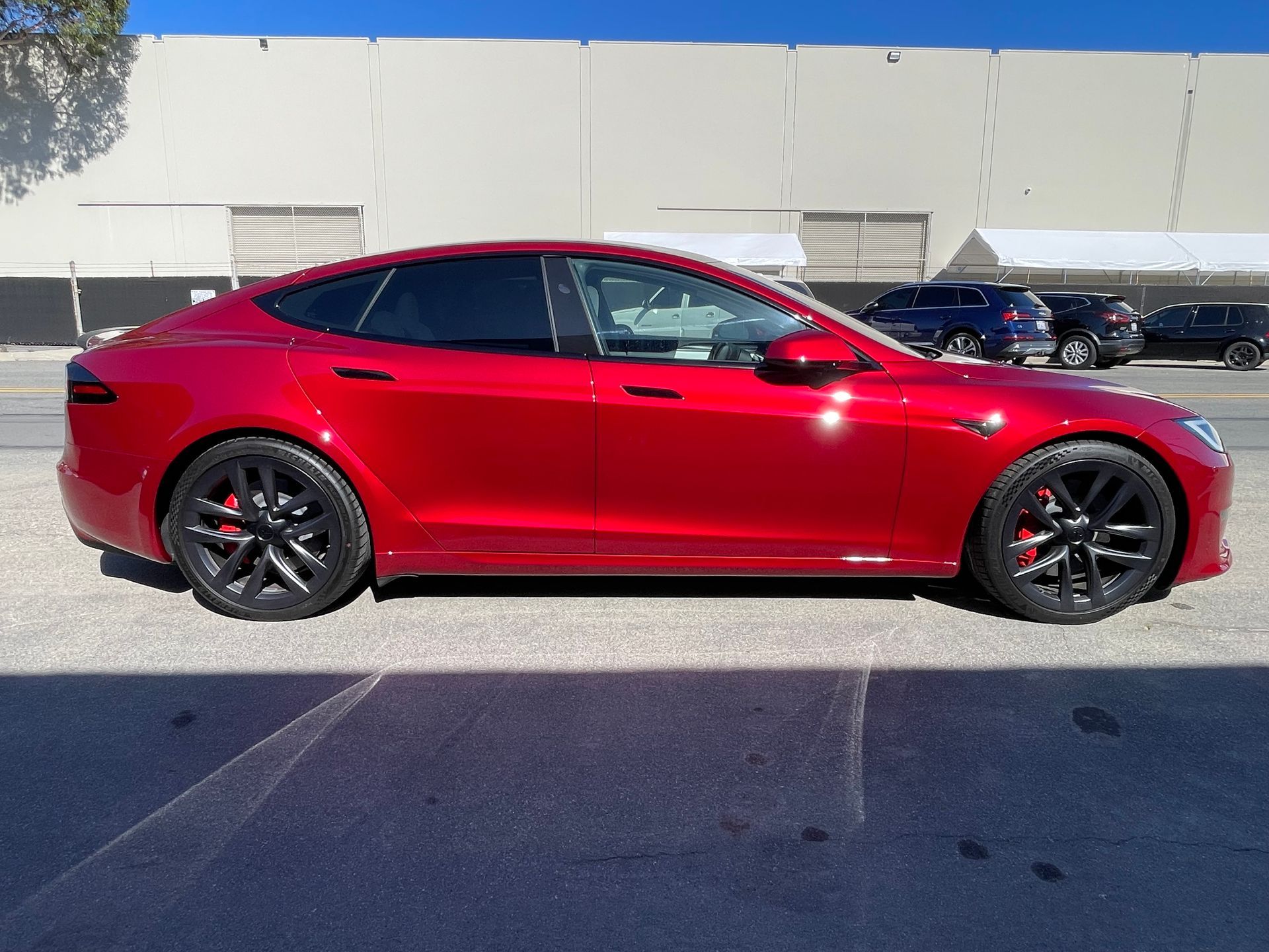 Red sedan parked in front of a beige building under a clear blue sky.