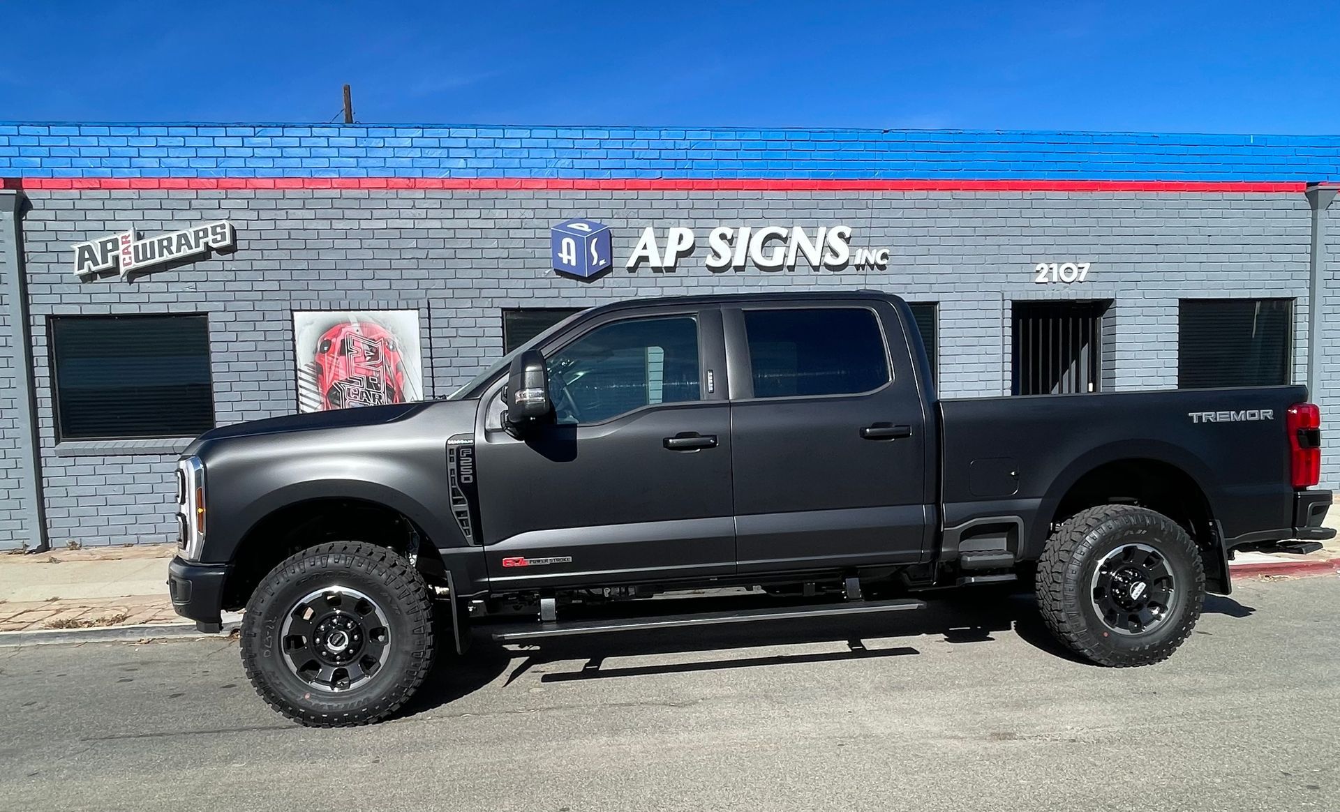 Black lifted pickup truck parked in front of an AP Signs building on a sunny street.