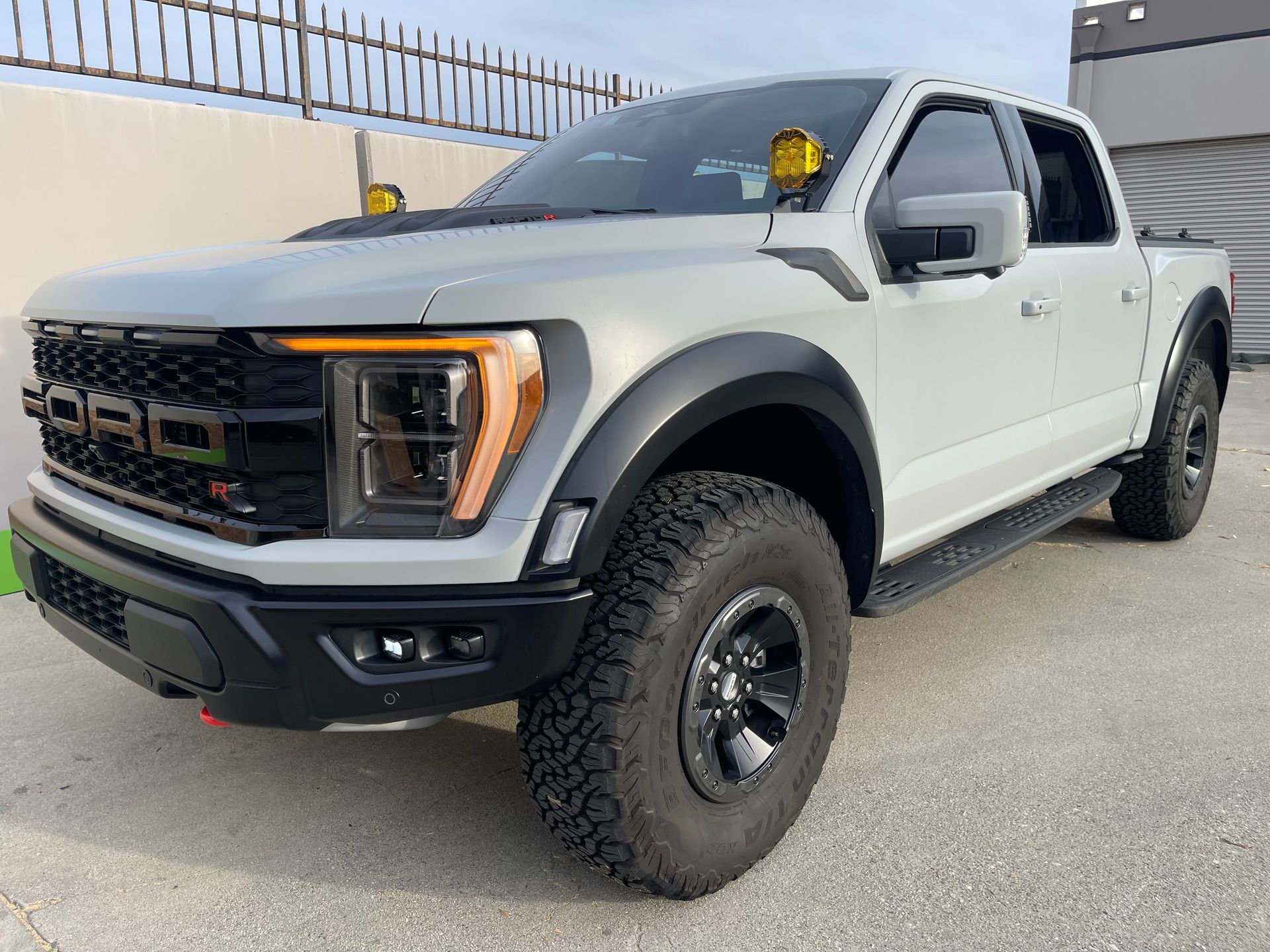 White lifted pickup truck parked outdoors on pavement near a fence, front three-quarter view