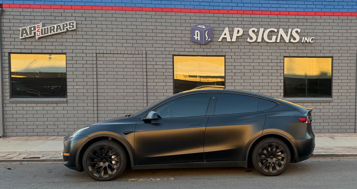 Black SUV parked in front of an A&P Signs storefront on a city street.