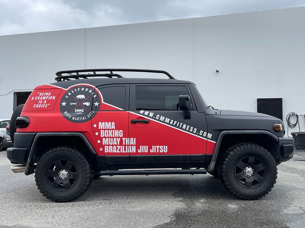 A red and black jeep is parked in front of a building.