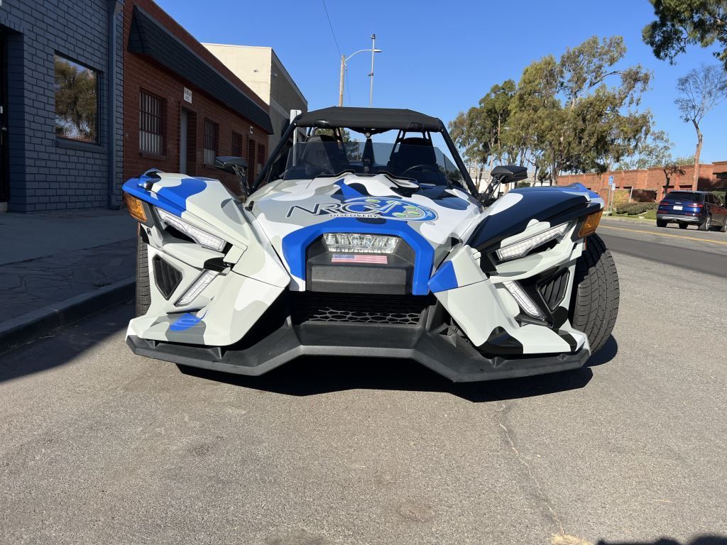 Polaris Slingshot trike with blue camo paint, parked on a city street.