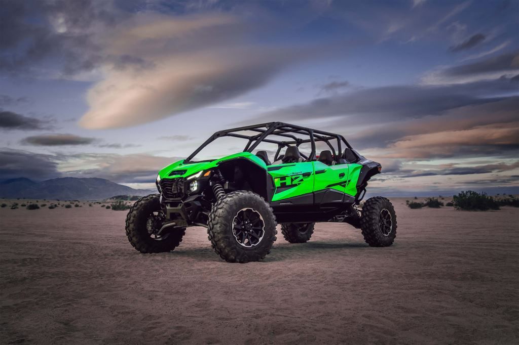 Green and black off-road vehicle in a desert setting with a cloudy sky in the background.