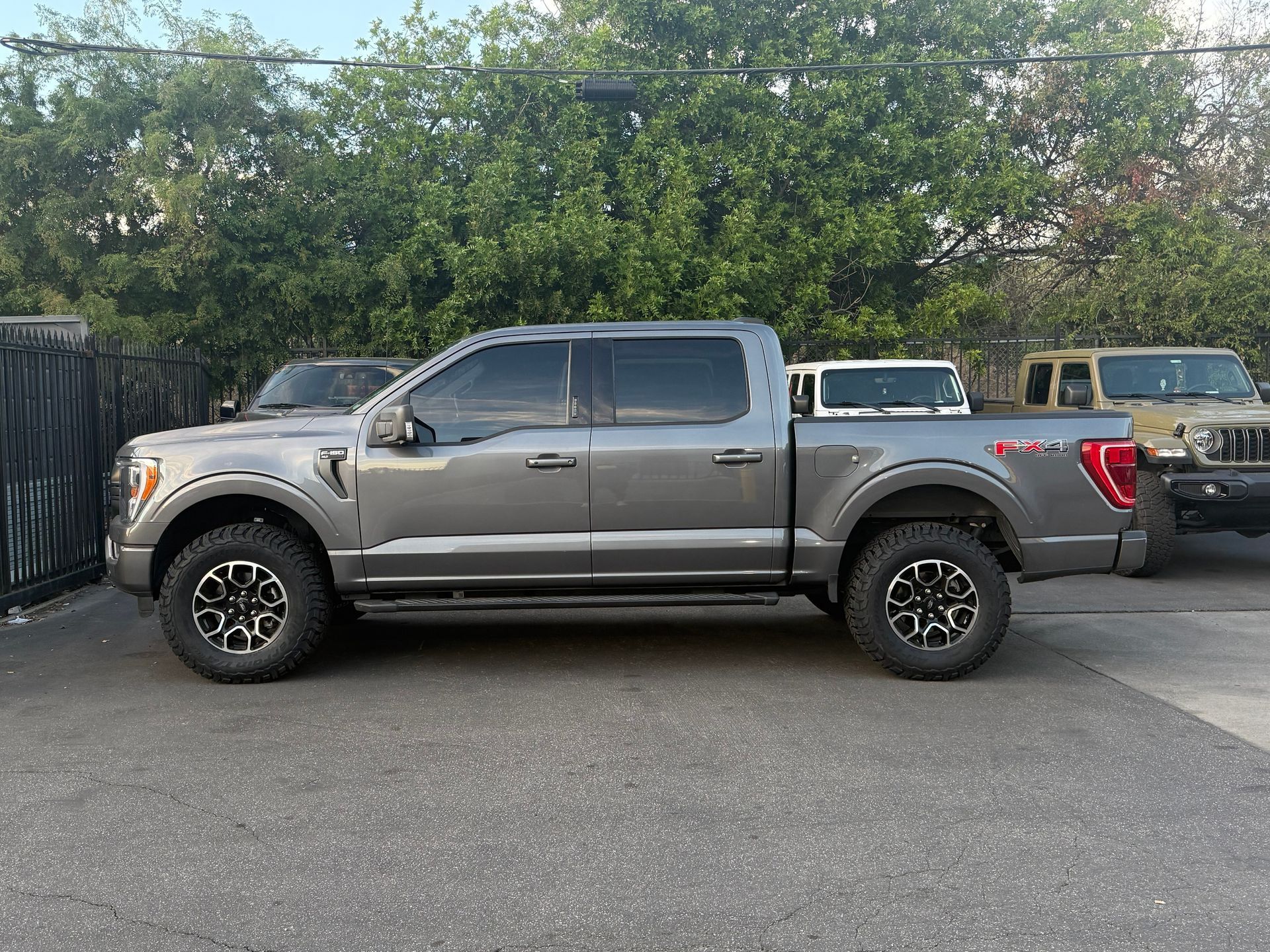 A silver pickup truck parked in a lot beside a fence and trees - Before