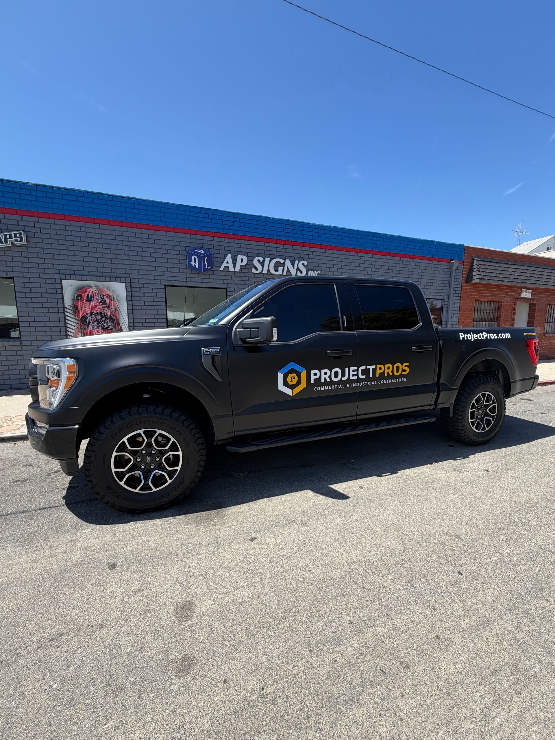 Black Project Frog pickup truck parked outside a brick building under a clear blue sky.