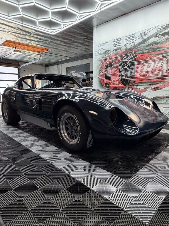 Black classic sports car in a showroom with checkered floor and wall murals