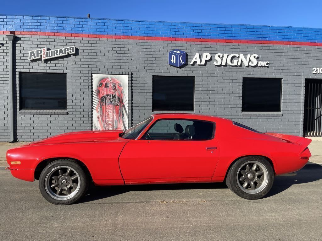 Red sports car parked in front of a gray brick auto shop with AP SIGNS signage