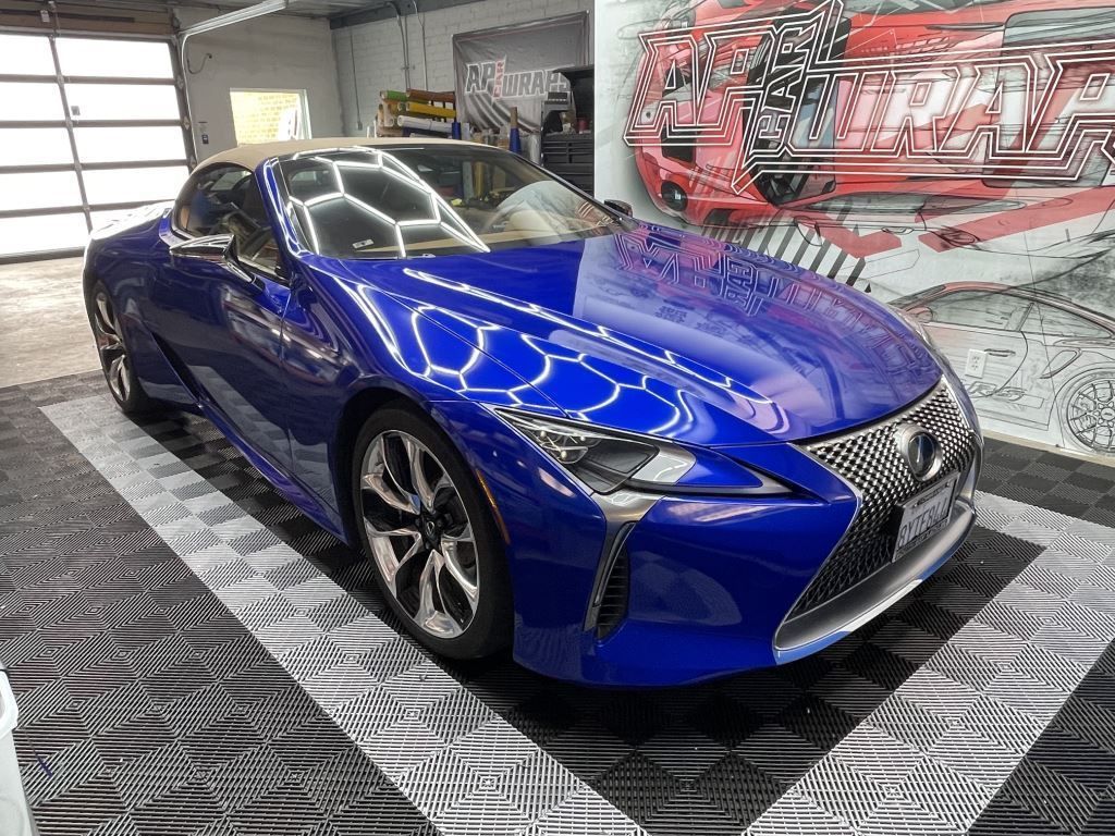 Blue Lexus sports car in a showroom on a checkered floor with a red sports car in the background