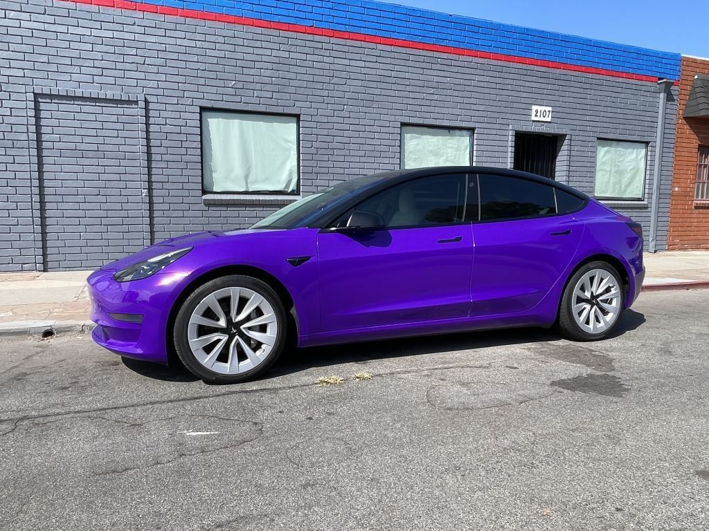 Purple sedan parked beside a gray brick building under a blue roofline.